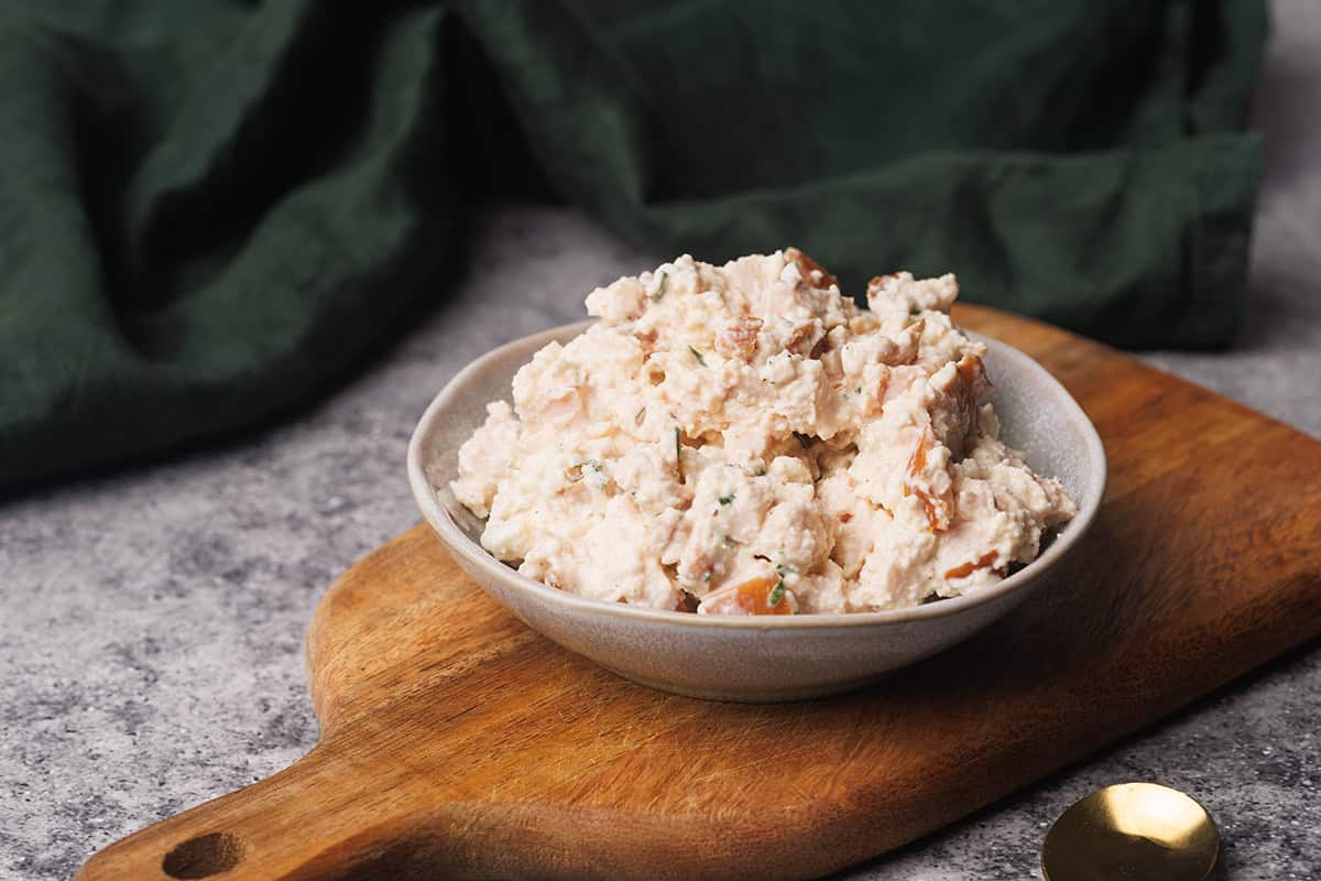 Smoked chicken salad in a small bowl on a wooden board.