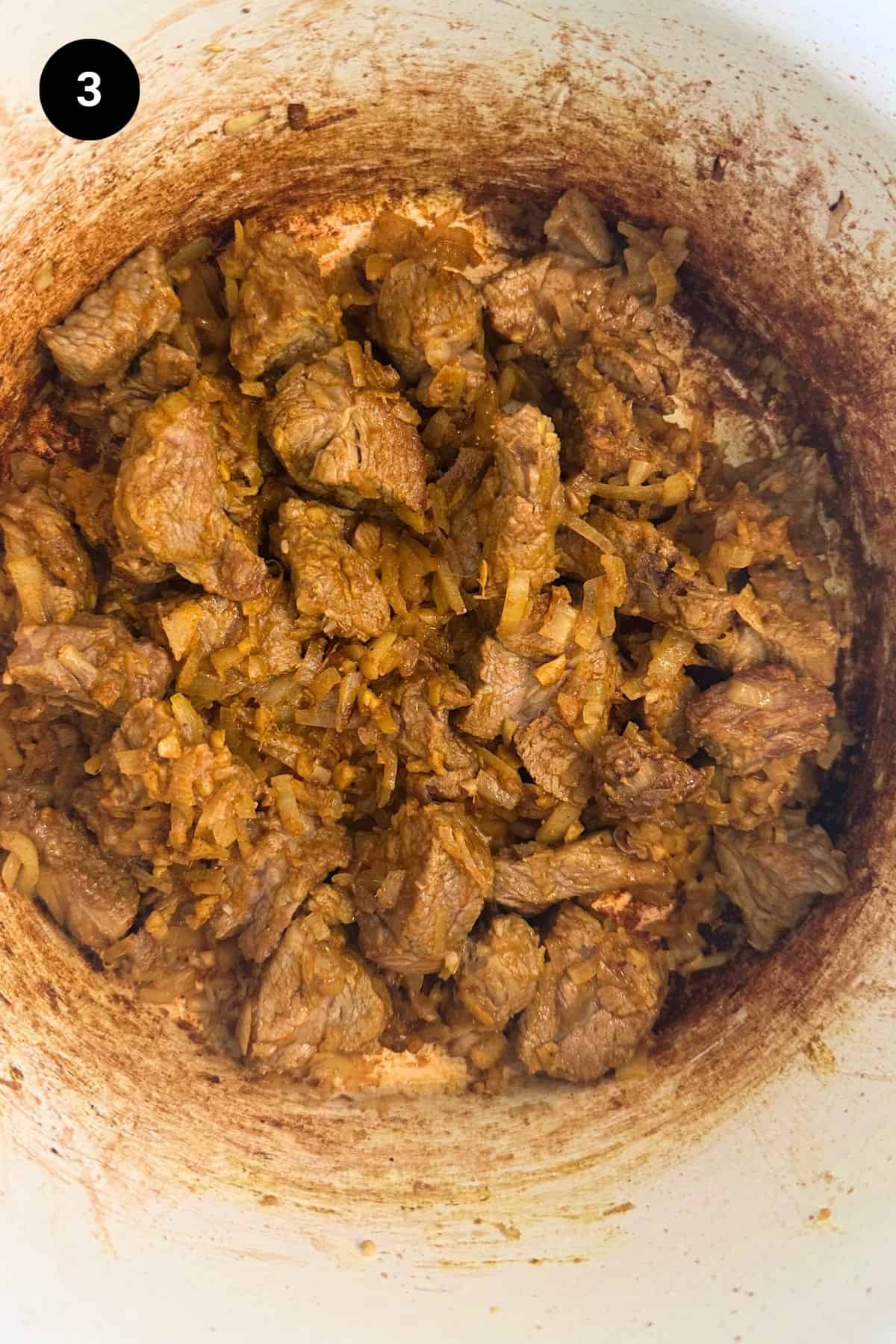 Diced lamb with seasonings in a Dutch oven.