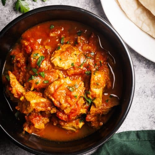 A black bowl filled with lamb curry next to naan bread and a green napkin.