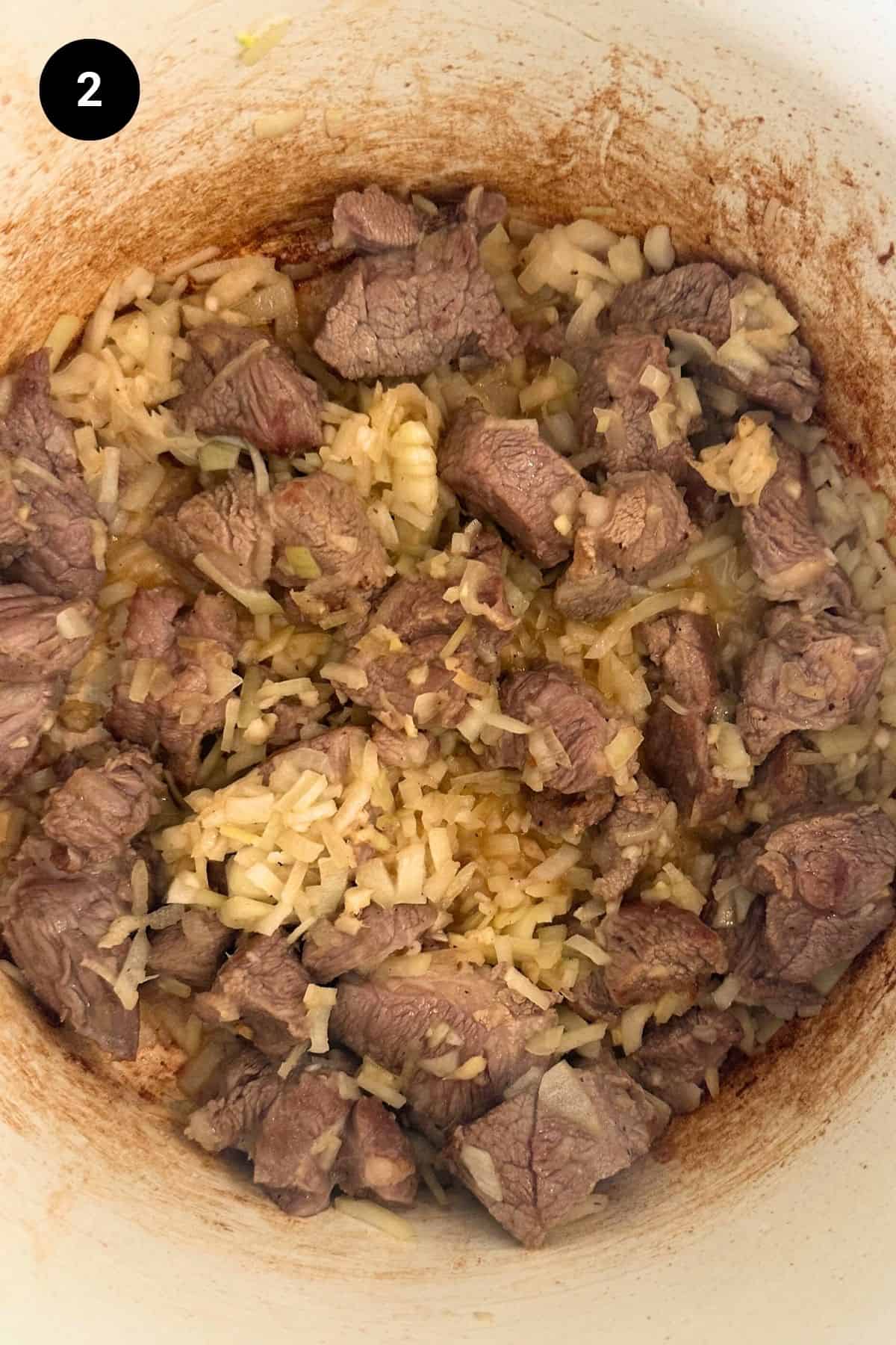 Diced lamb and onion in a Dutch oven.