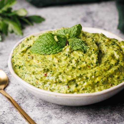Mint pesto in a small white bowl next to a green napkin and golden spoon.