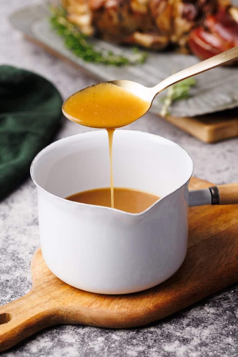Lamb gravy in a small white saucepan on a wooden board.