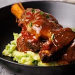 Lamb shanks on mashed peas and potatoes in a black bowl.