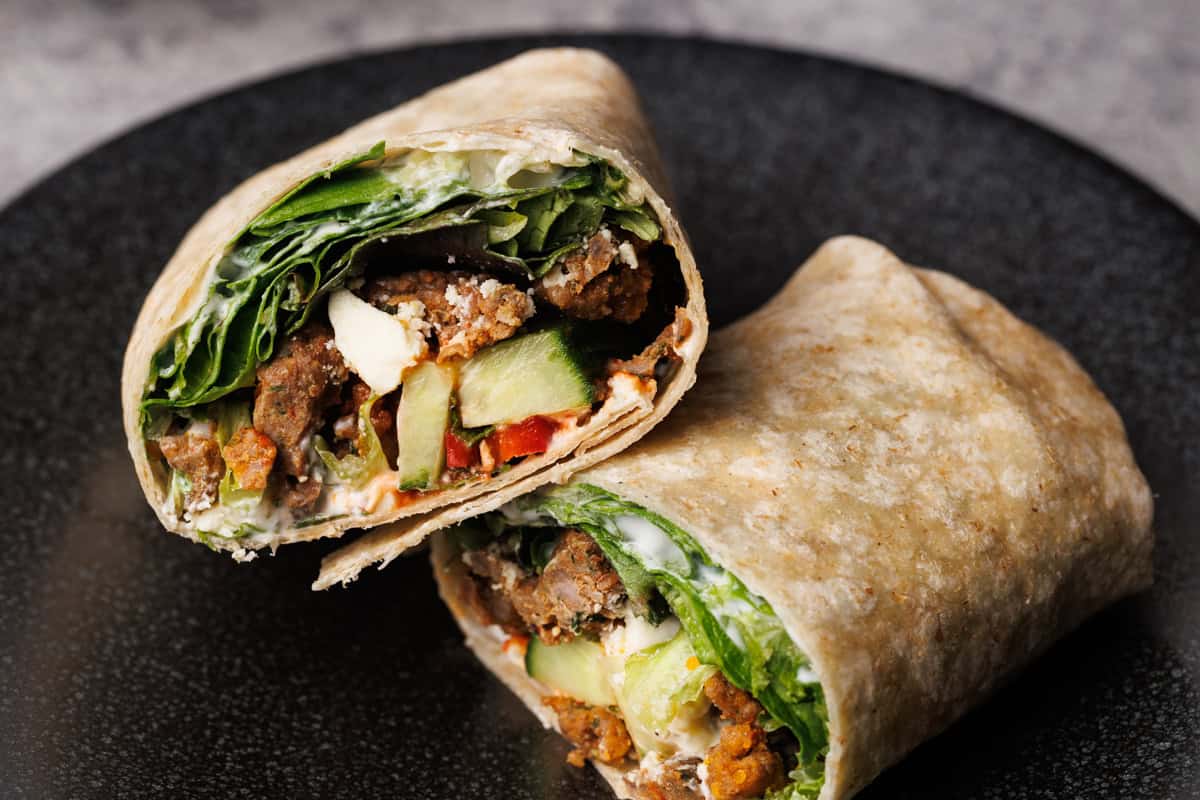 A lamb wrap cut in half on a black plate.
