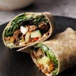A lamb wrap cut in half on a black plate.