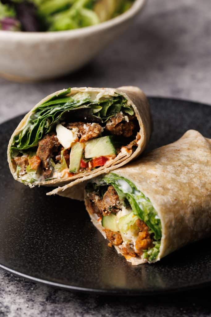 A lamb wrap cut in half on a black plate.