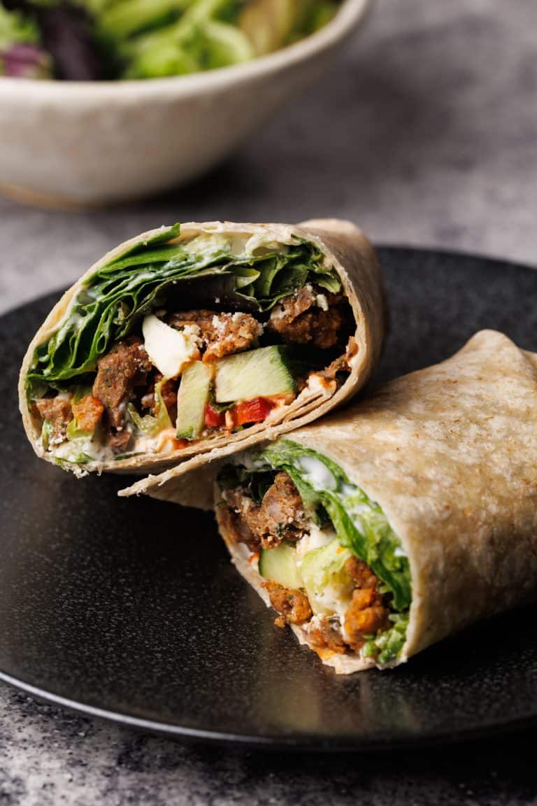 A lamb wrap cut in half on a black plate.