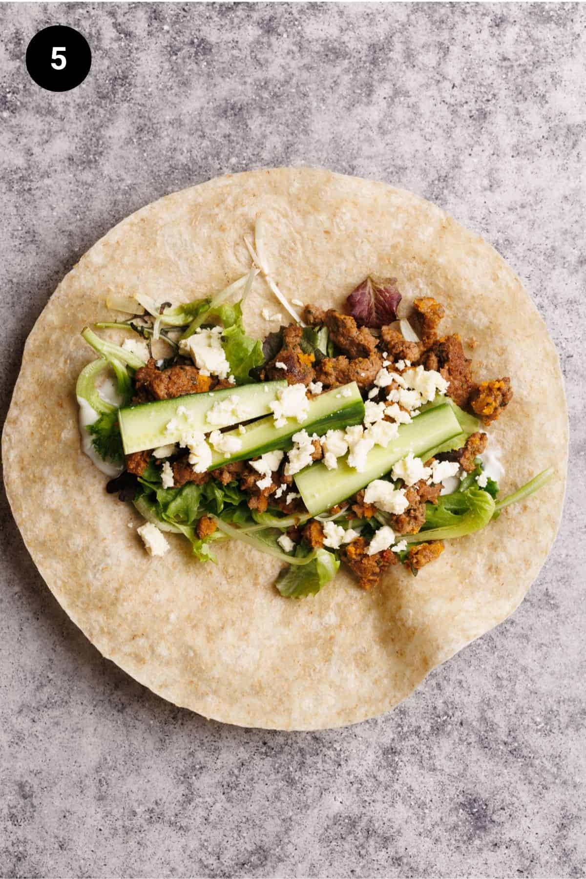 Salad, cucumber, feta, and cooked sausage on a flour tortilla.