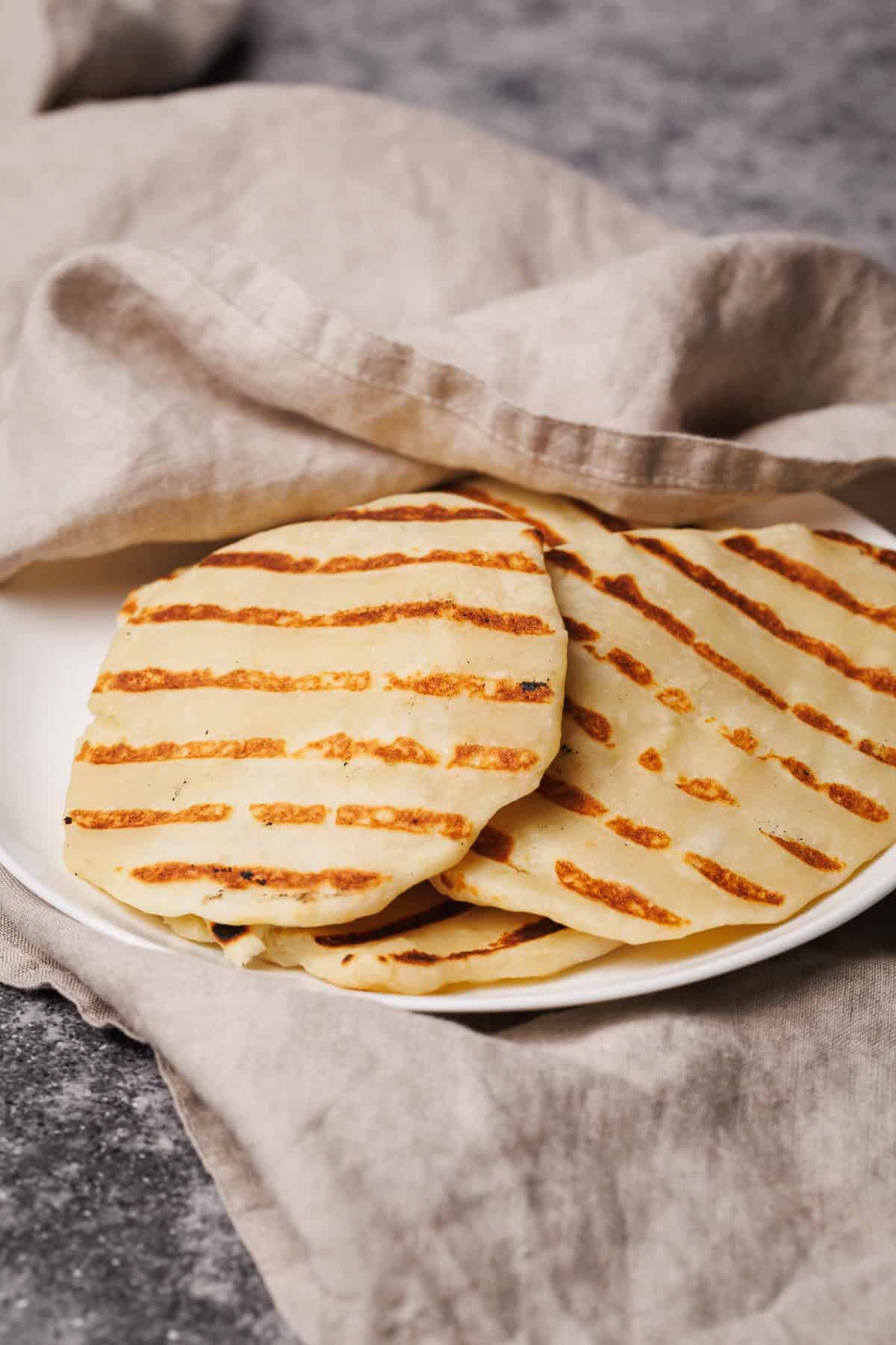 Flatbreads on a white plate covered in a natural linen tea towel.