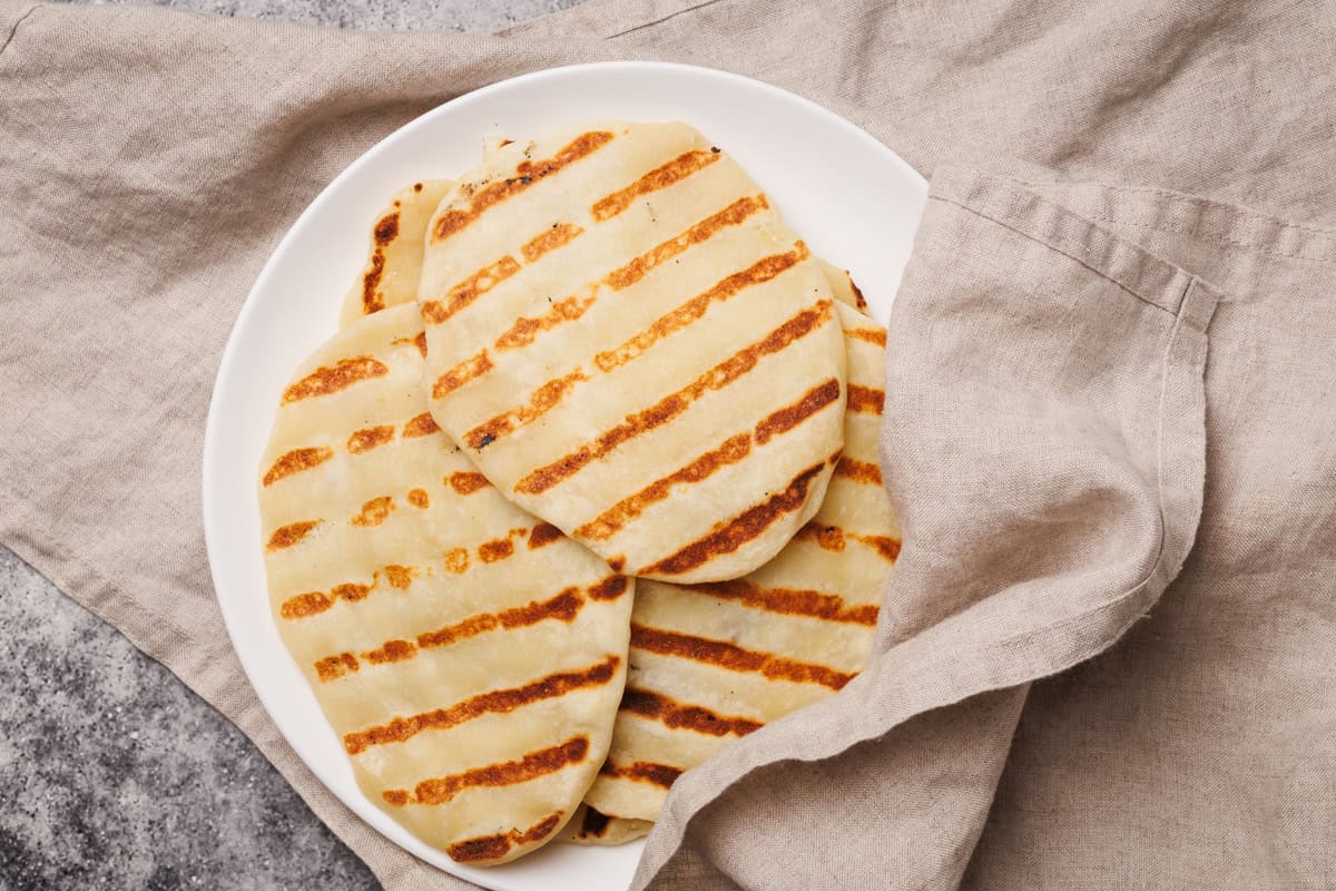 Flatbreads on a white plate covered in a natural linen tea towel.