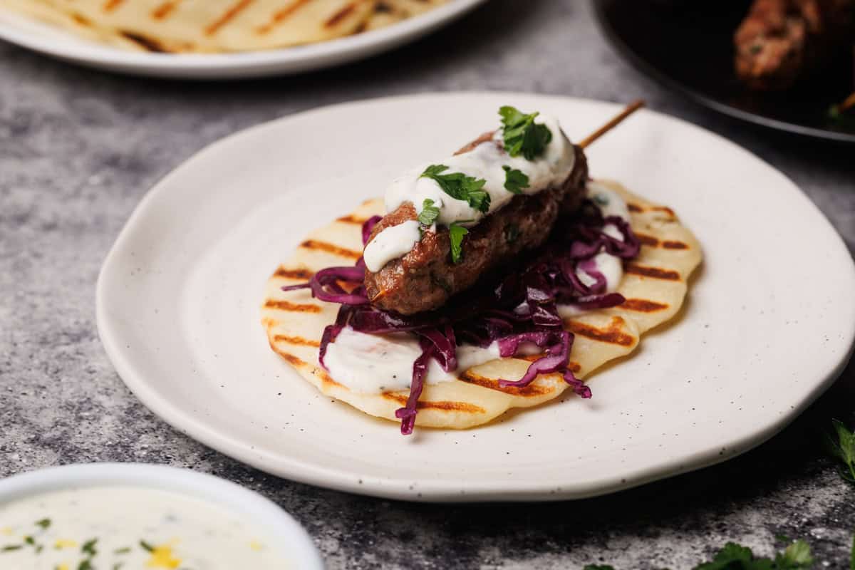 Lamb kebab on a white plate next to meal components.