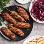 Lamb kofta on a black plate next to meal components.