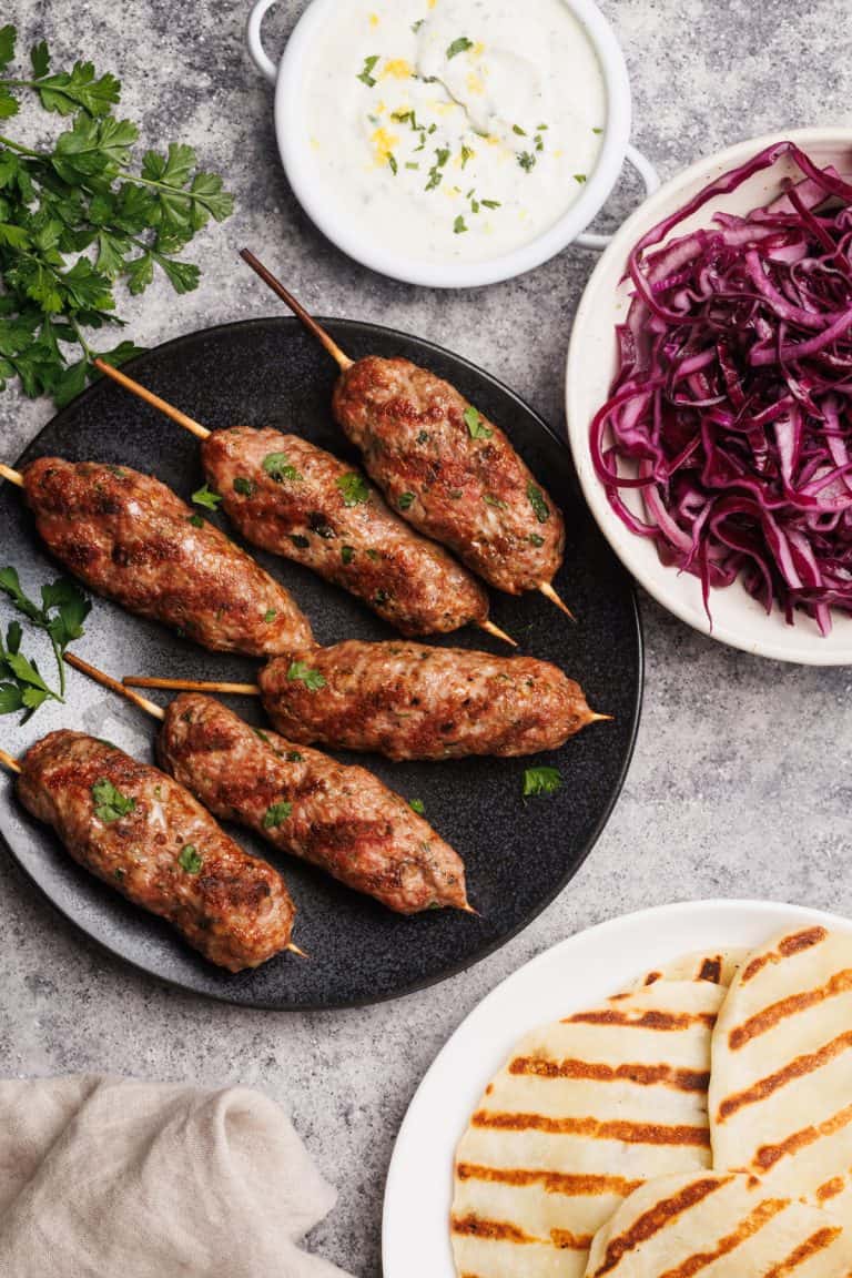 Lamb kofta on a black plate next to meal components.