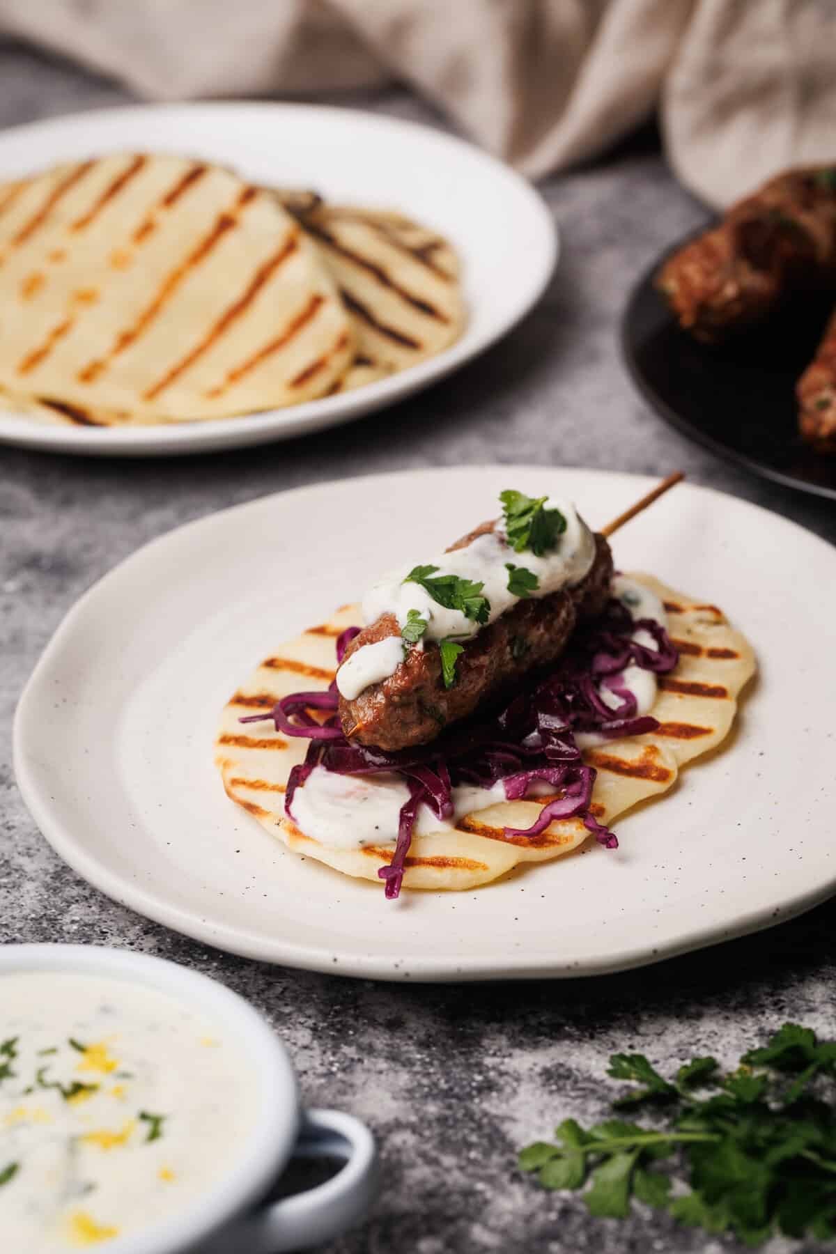 Lamb kebab on a white plate next to meal components.