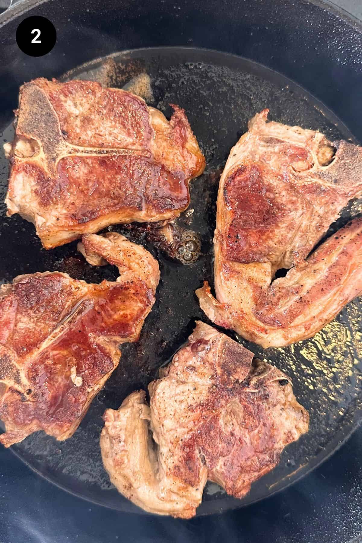 Lamb chops being seared in a cast iron skillet.