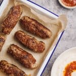 An enamel tray with lamb sausages next to dips.