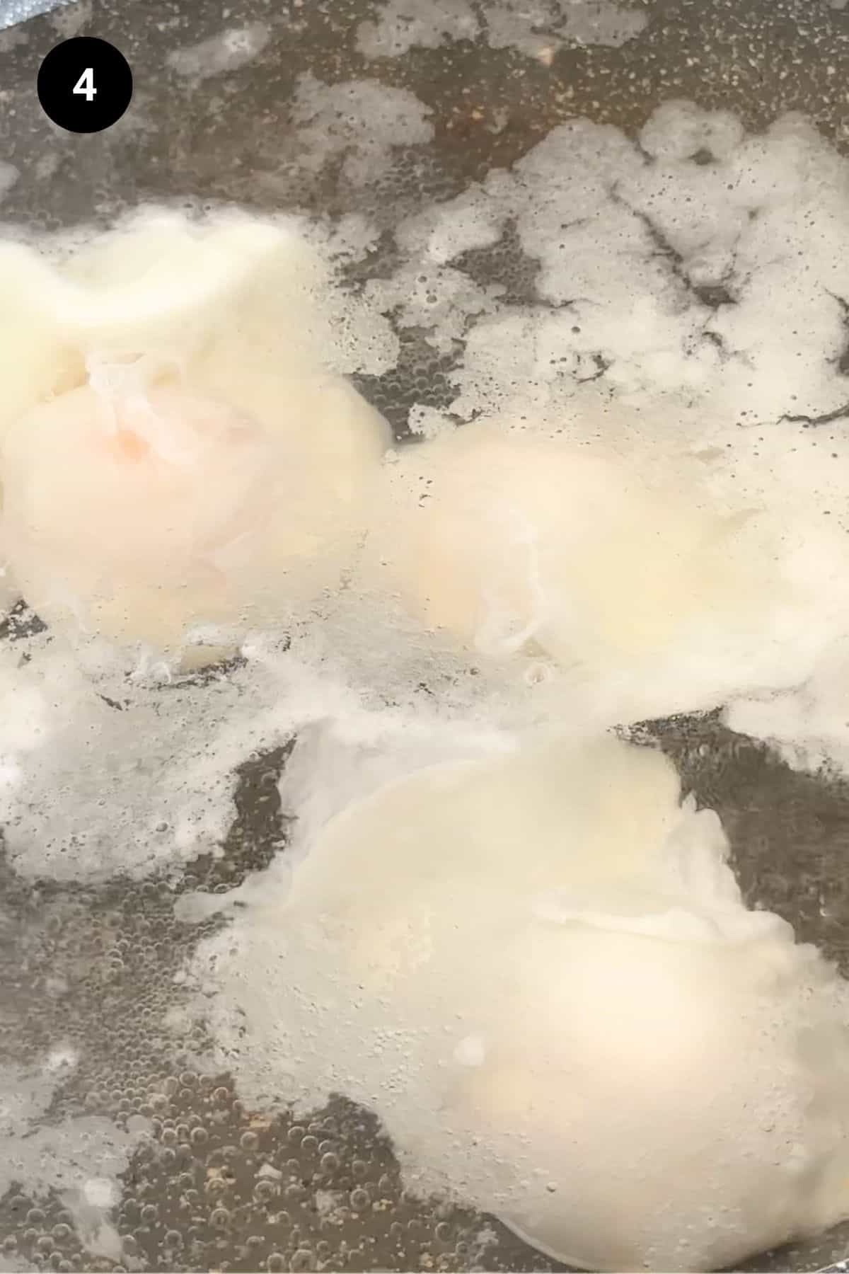Eggs being poached in a grey pan.