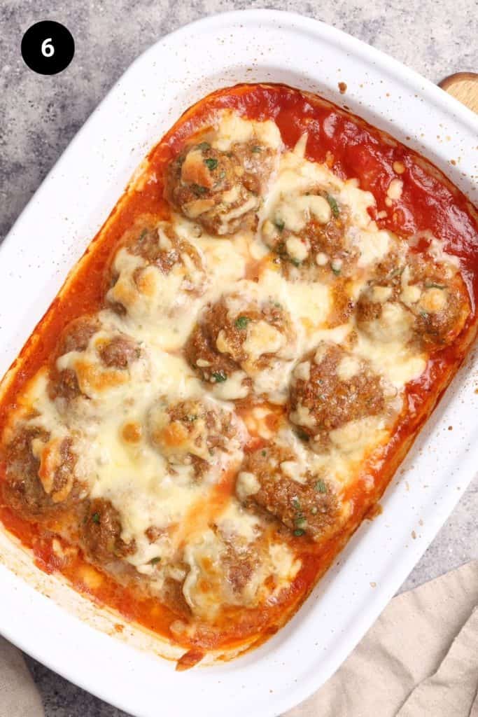 Baked harissa meatballs in a white casserole dish next to a linen tea towel.