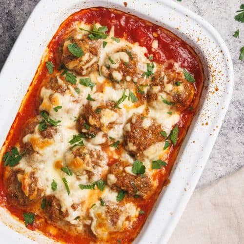 Baked meatballs in a white casserole dish next to a linen tea towel.