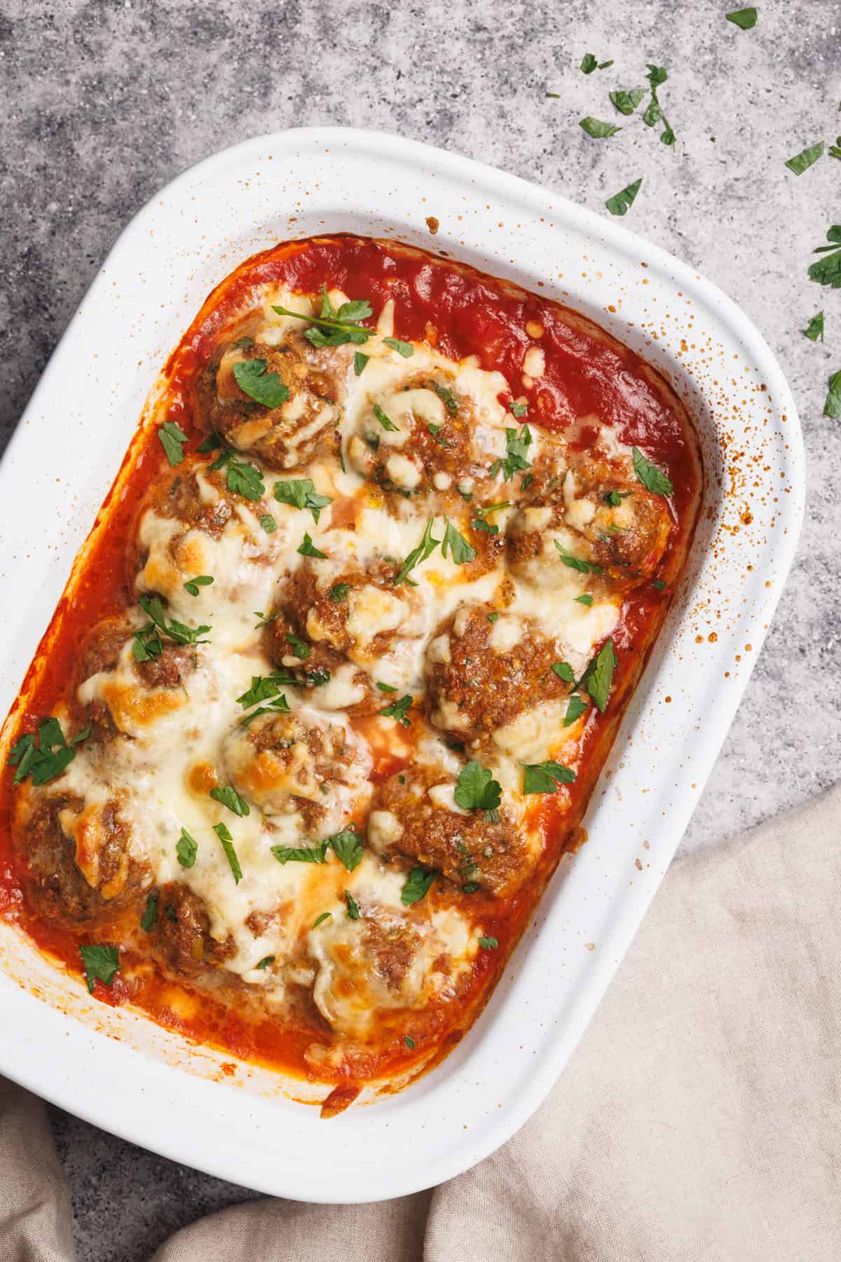 Baked meatballs in a white casserole dish next to a linen tea towel.