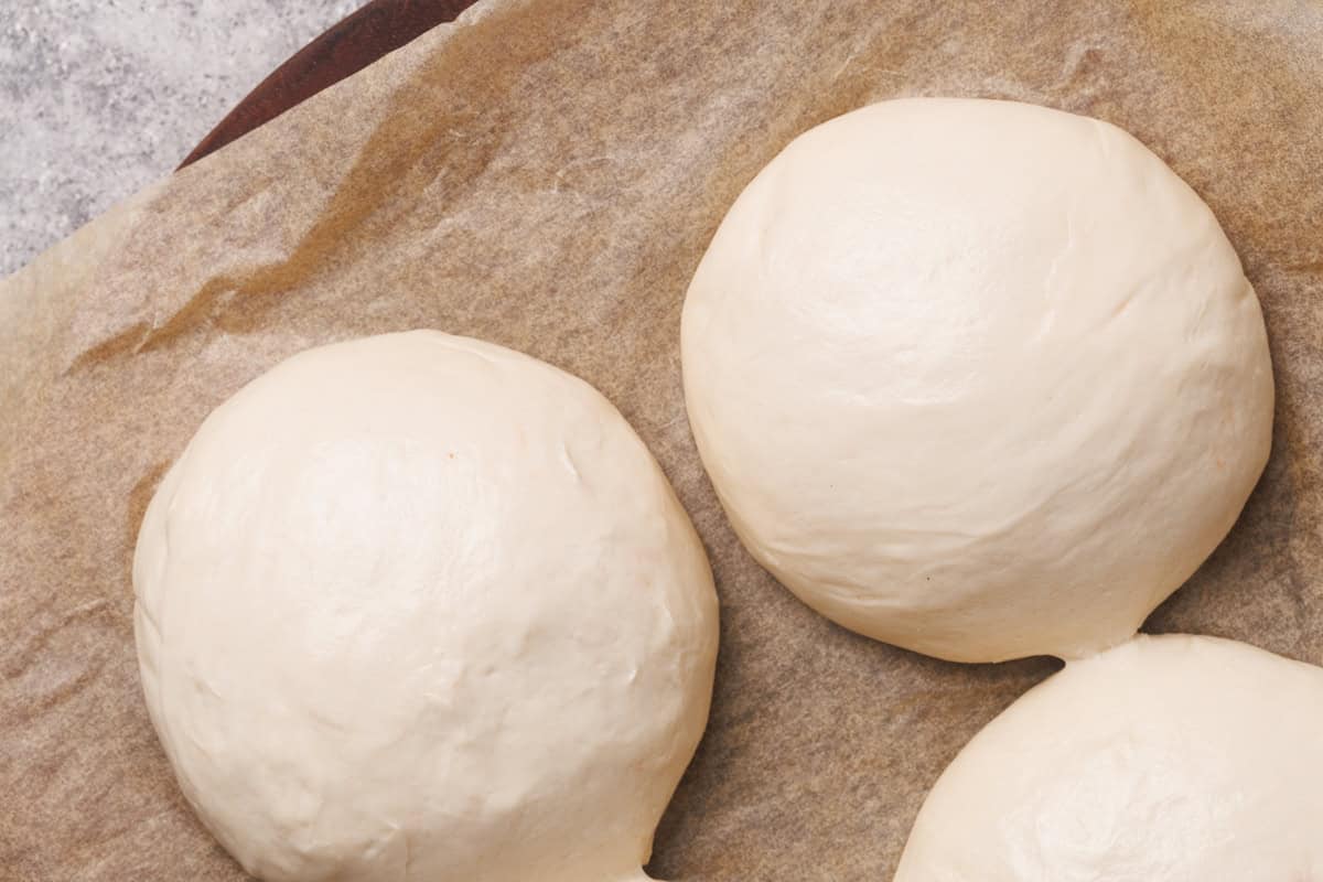 Three pizza dough ball on brown baking paper.