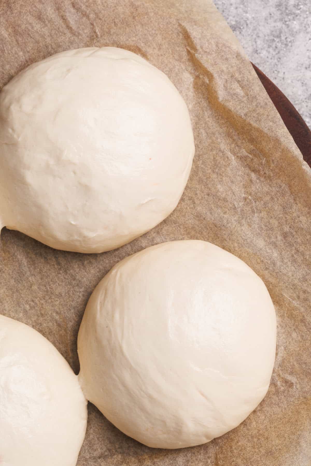 Three pizza dough ball on brown baking paper.