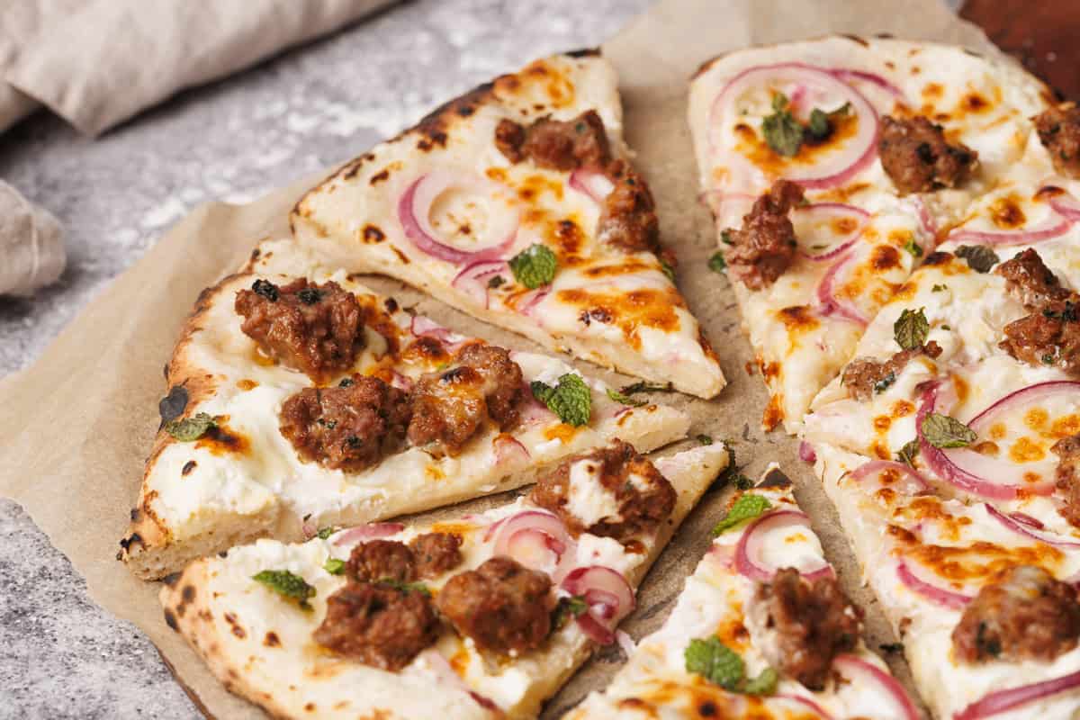 Sliced German pizza on a baking paper lined wooden board next to a linen napkin.