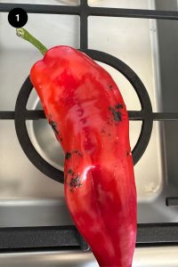 Red pepper being charred on a gas stove.