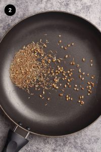 Whole seeds being toasted in a black pan.
