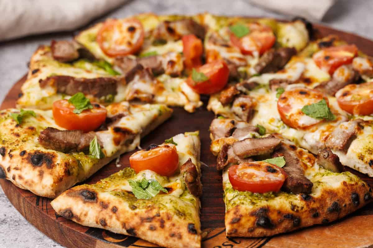 A baked lamb pesto pizza on a wooden board next to a linen napkin.