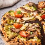 A baked pesto pizza on a wooden board next to a linen napkin.
