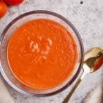 Pizza sauce in a glass bowl next to fresh tomatoes, a napkin, and black pepper.