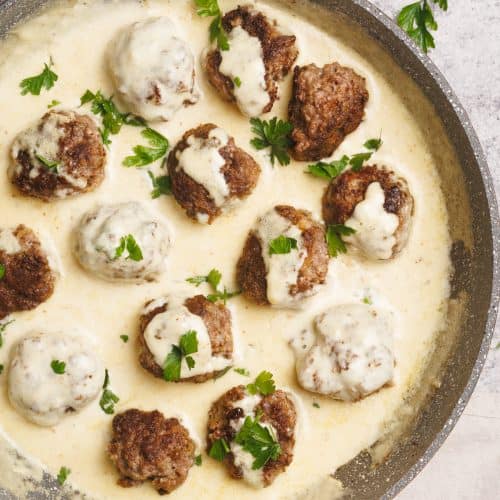 Alfredo sauce with meatballs in a large pan next to some fresh parsley on a concrete background.