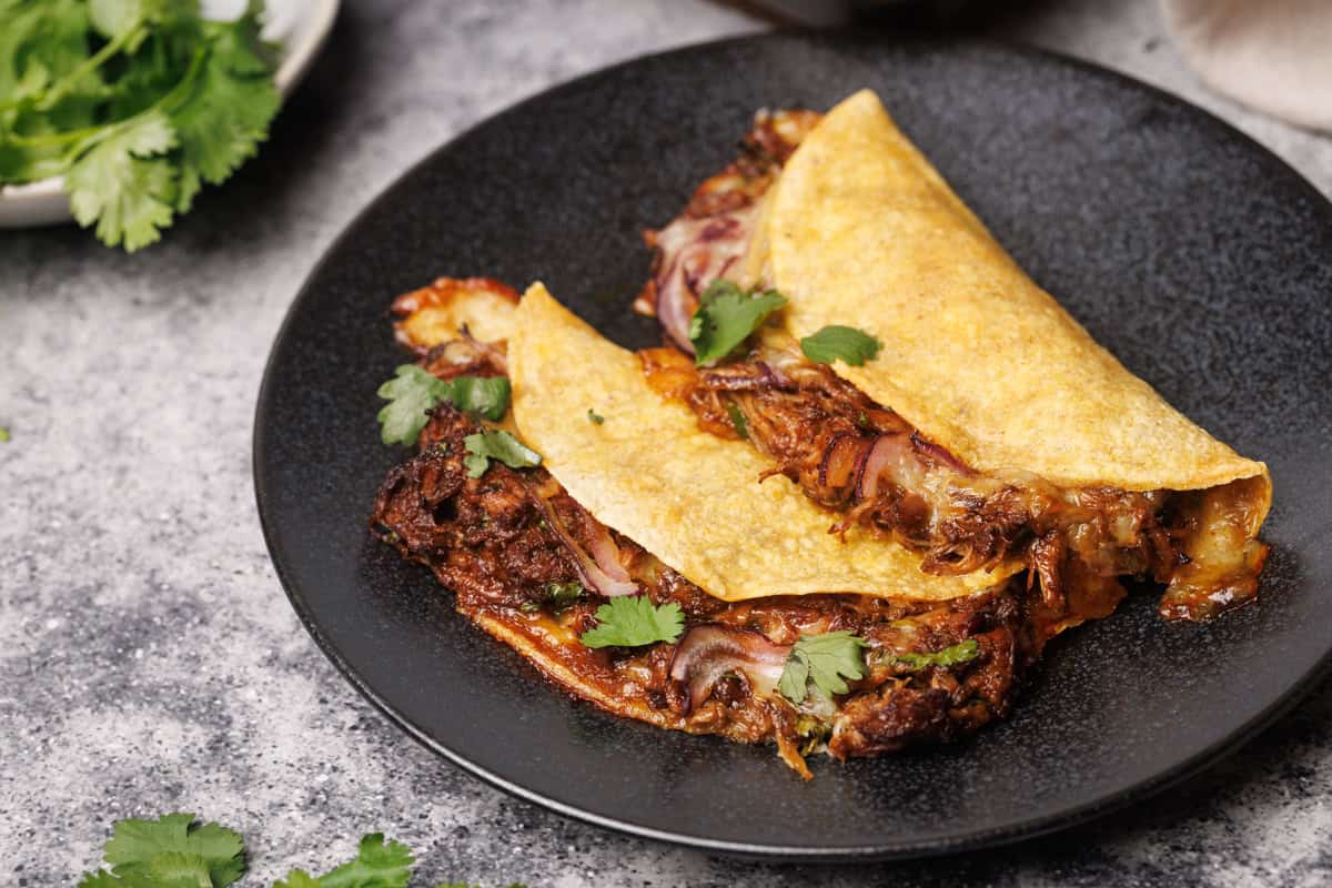 Two baked birria quesadillas on a black plate.