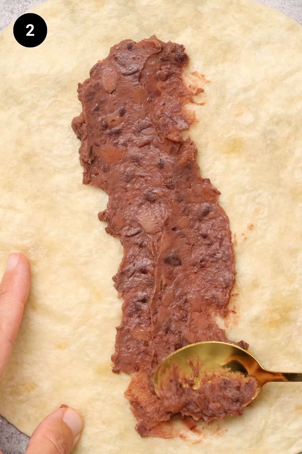 Refried beans added to tortilla.