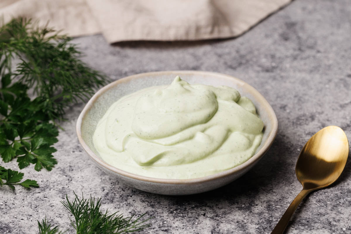 Ranch dip in a small bowl next to fresh herbs and a linen tea towel.