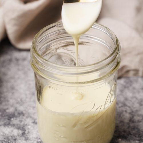 A mason jar with evaporated milk and a spoon spooning it out.