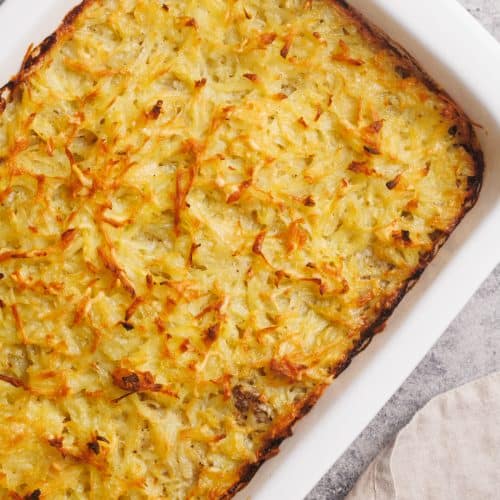 Hash brown beef casserole in a white casserole dish next to a linen towel.