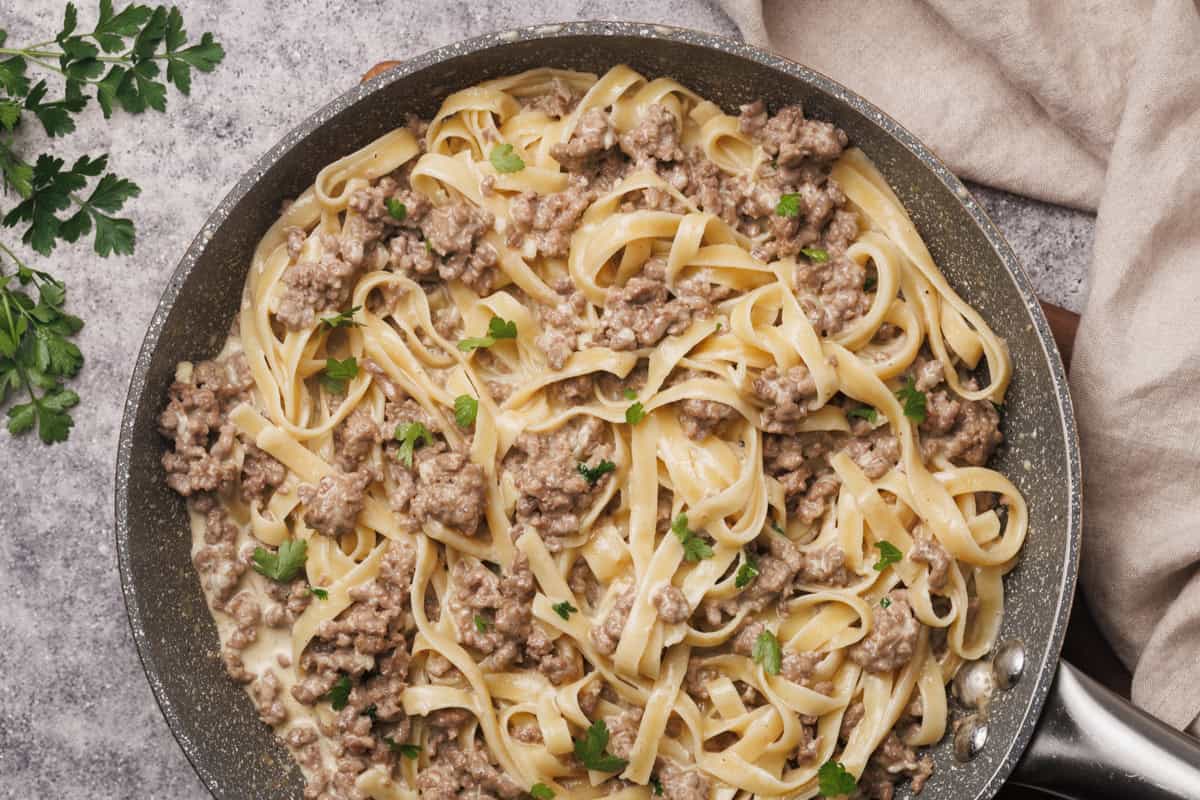 Hamburger Alfredo in a grey pan next to a tea towel and fresh parsley.