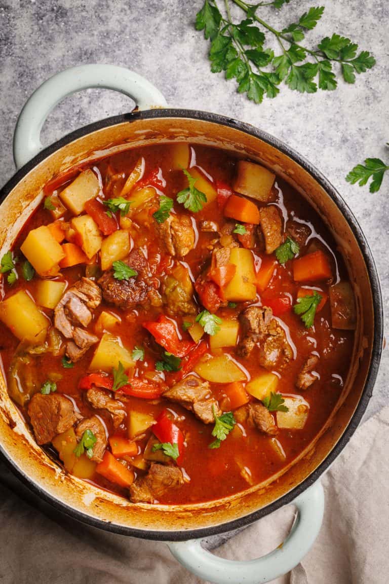 A Dutch oven filled with Hungarian goulash next to parsley.