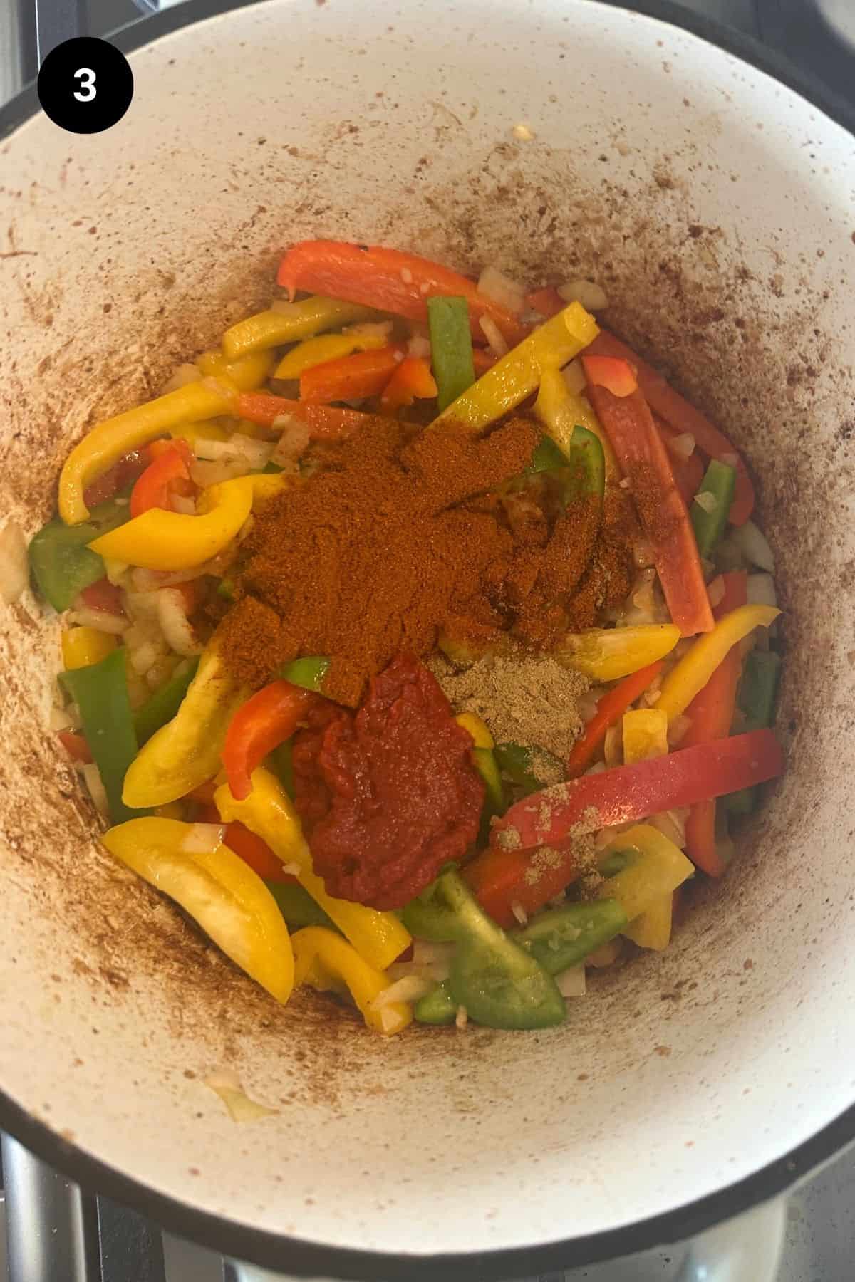 Spices on top of red peppers in a Dutch oven.