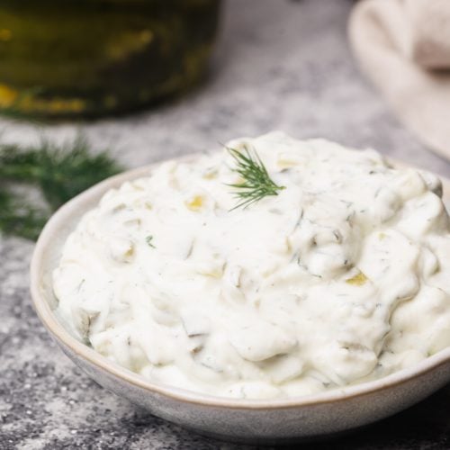 Pickle sauce in a small bowl next to fresh dill and gherkins.