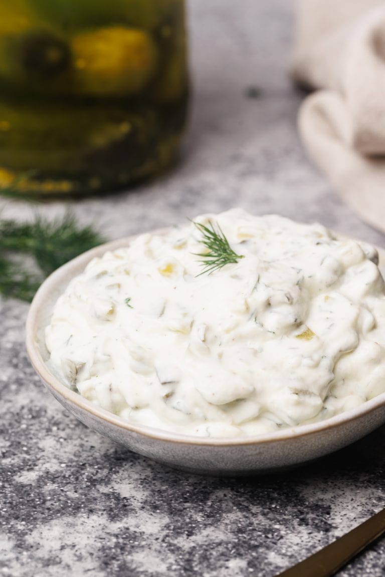 Pickle sauce in a small bowl next to fresh dill and gherkins.