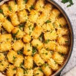 Top down view of the tater tot casserole next to a linen tea towel and fresh parsley.