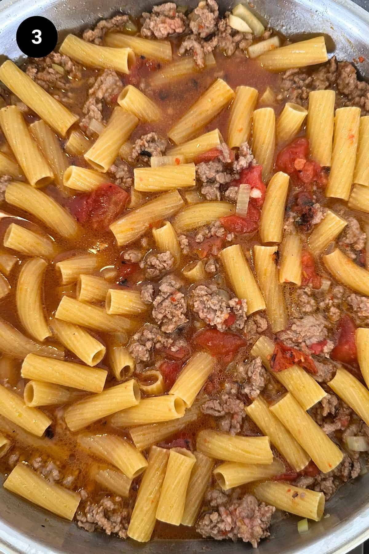 Uncooked pasta added to the ground beef and tomato.