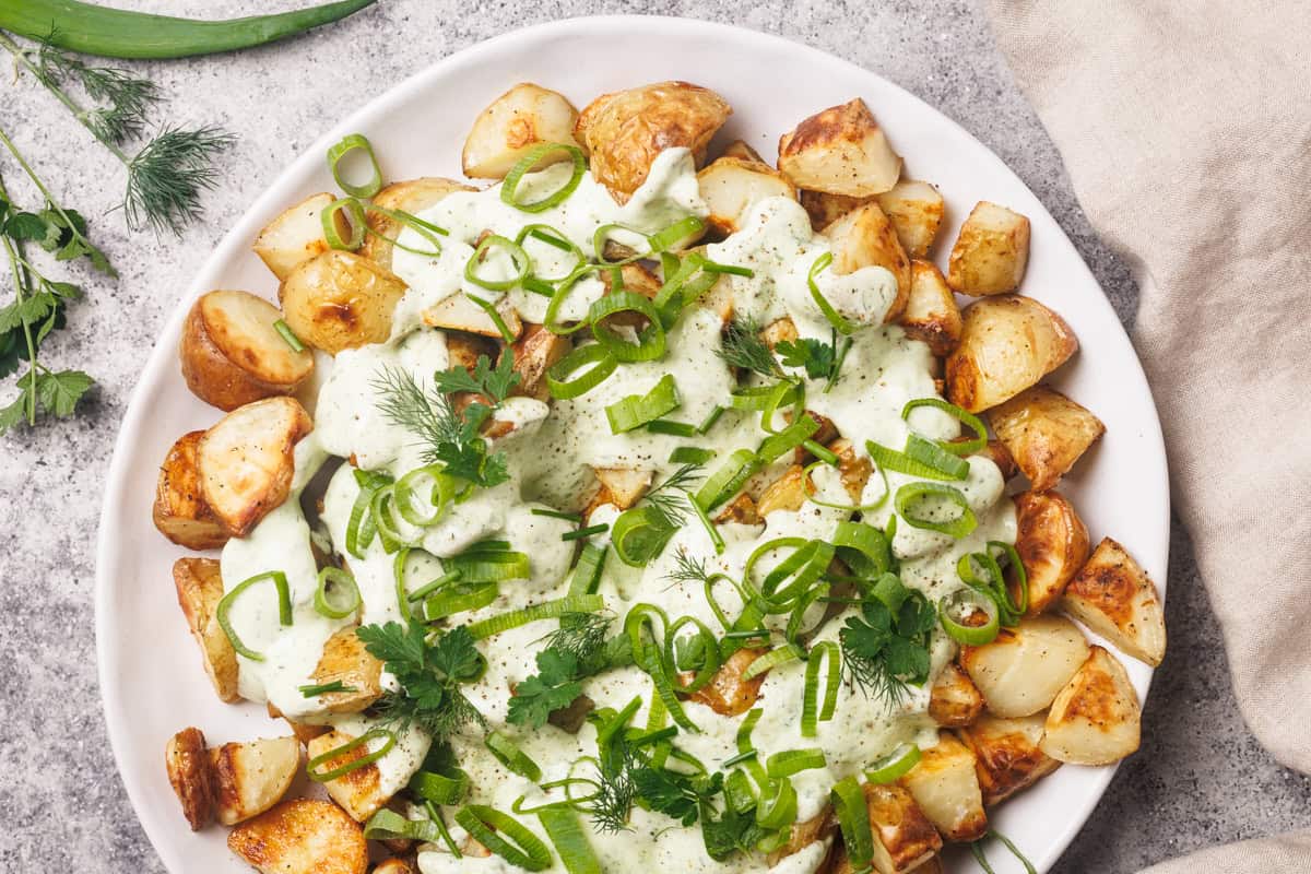A white plate with loaded ranch potatoes next to a linen tea towel.