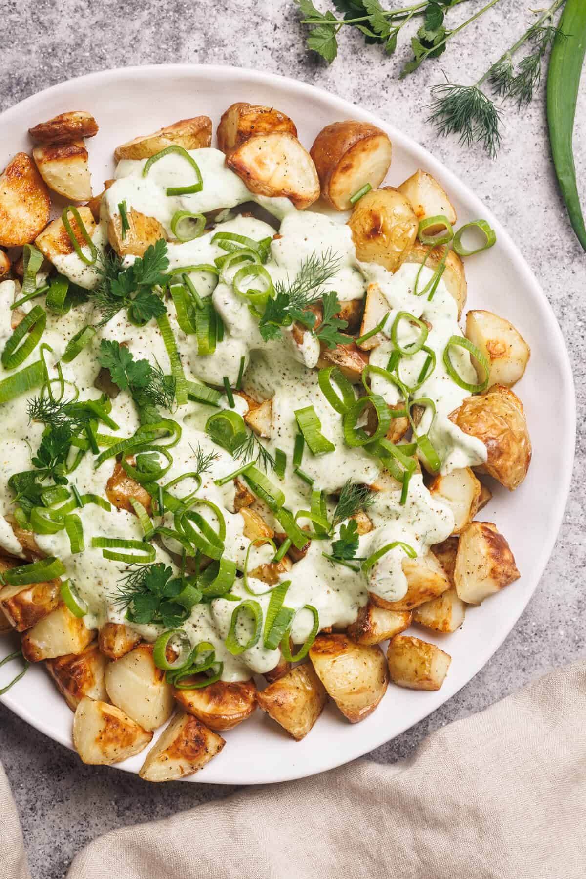 A white plate with loaded ranch potatoes next to a linen tea towel.