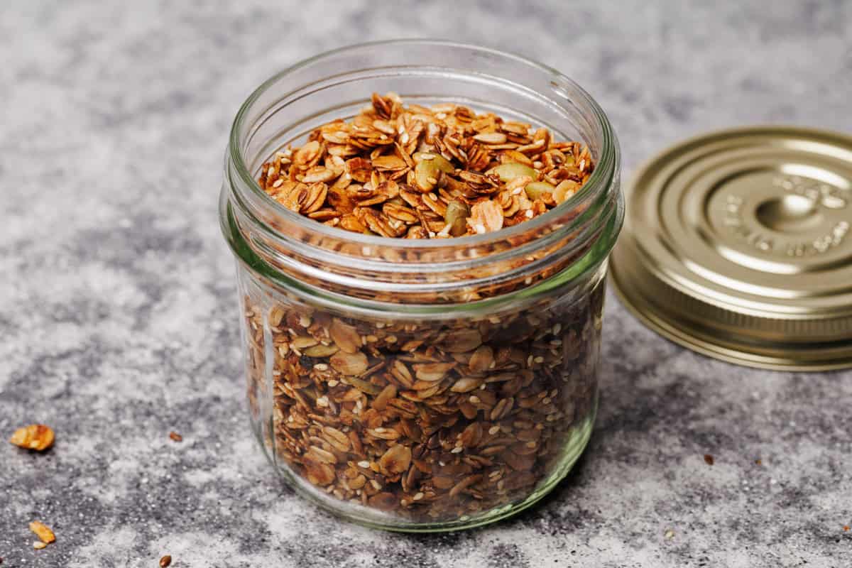 A glass jar with olive oil granola with the lid next to it.