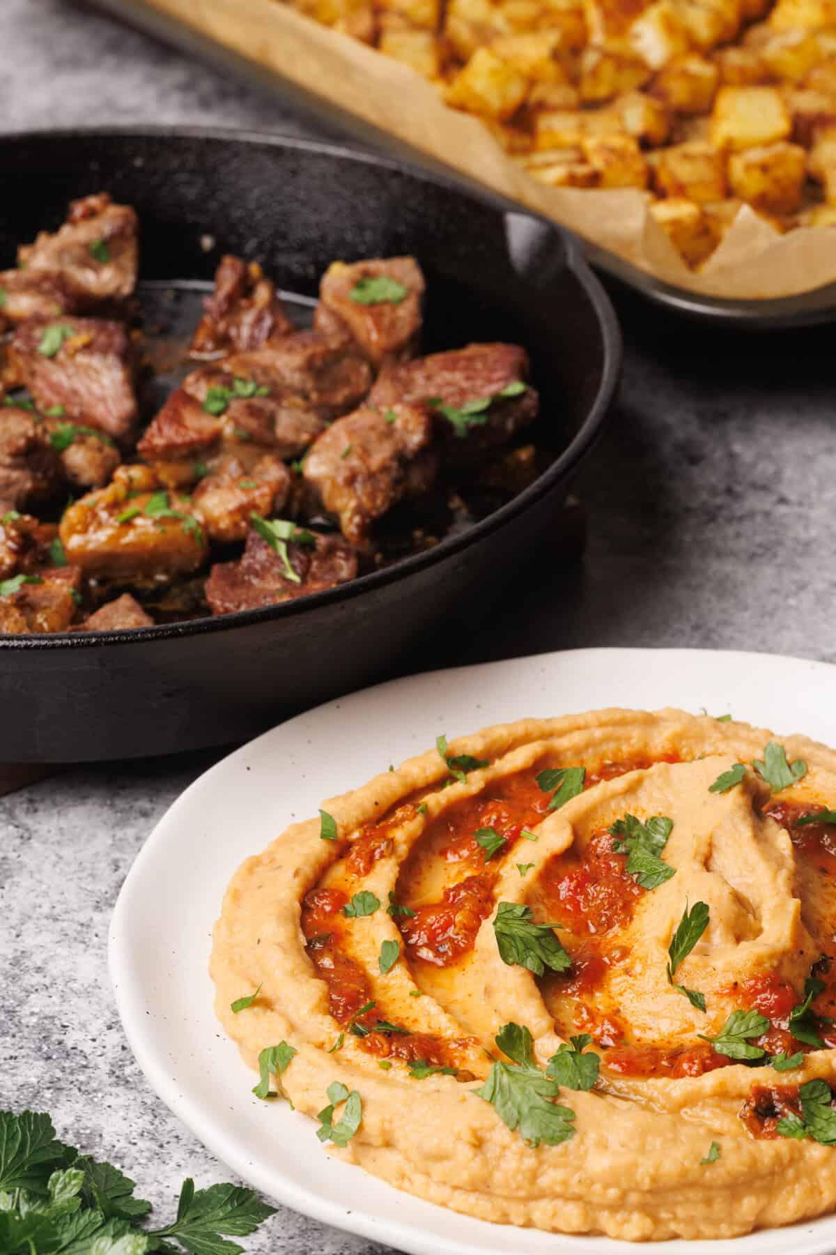 Harissa hummus next to steak bites and potatoes.