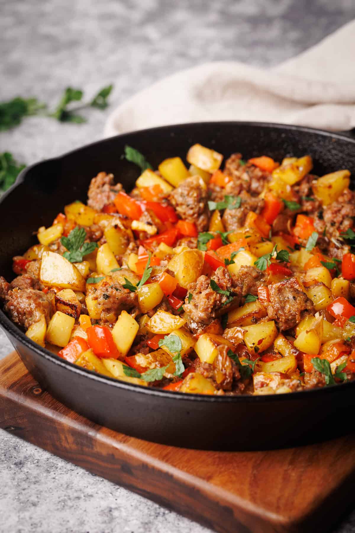 Sausage and potato hash in a cast iron pan next to a linen towel and fresh herbs.